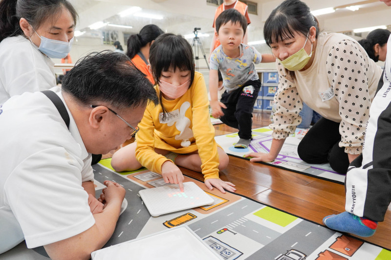 中華民國遊戲協會理事長林君英（左1）向孩子示範玩具的玩法，家長在一旁學習。（新北市社會局提供）