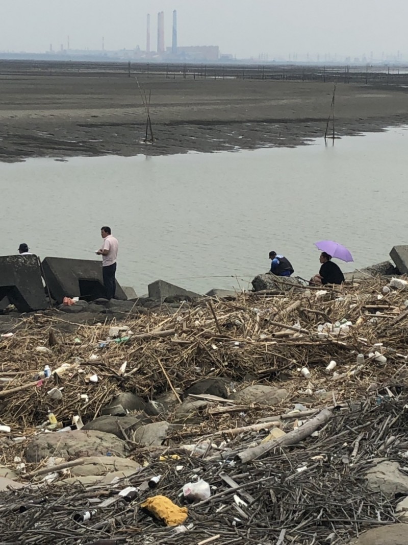 釣客踩過垃圾山蹲在垃圾堆裡釣魚，民眾嘲諷此景成世界奇景，「伸港獨有」！（記者張聰秋翻攝）