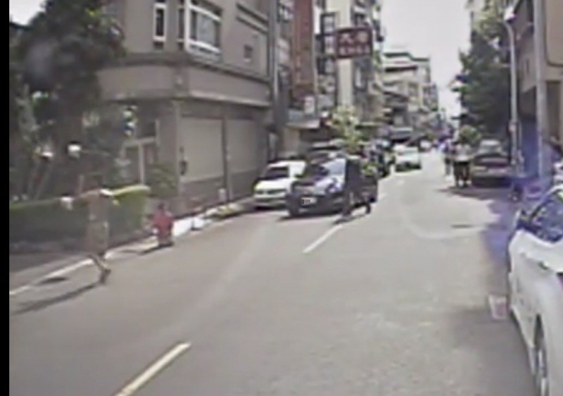孫男（左）逞凶後，仍當街拿著停車告示牌揮舞。（記者許國楨翻攝）