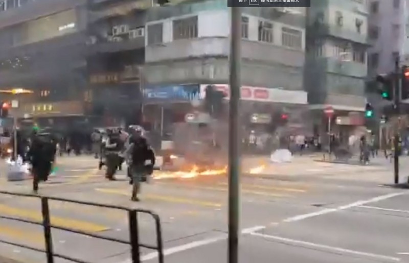 香港記者紀錄下警方在街頭閃過火堆，整隊人馬追趕示威者的景象。（擷取自「Hong Kong Free Press」推特影片）