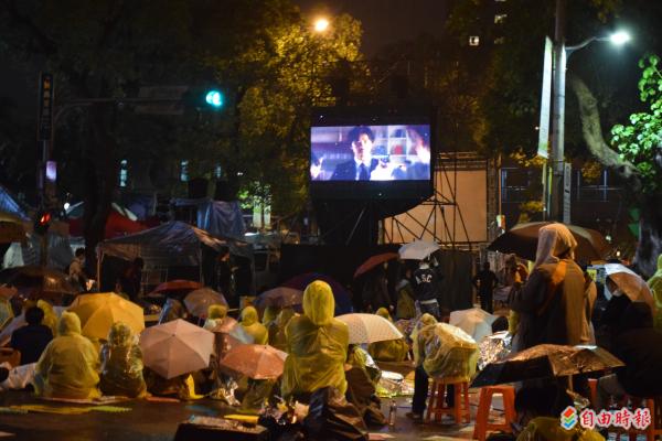 立法院外青島東路上放映日本電影《圖書館戰爭》，許多學生穿著雨衣冒雨在馬路上觀看。（記者陳韋宗攝）