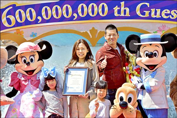 在夫婿、兩個女兒與眾多迪士尼知名卡通人物的簇擁下，來自名古屋的阪井有美（中）12日歡喜成為造訪東京迪士尼的第6億名遊客。（法新社）
