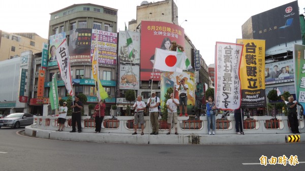 公投護台灣聯盟嘉義旗隊在嘉市地標中央噴水圓環舉旗歡迎田邊憲司，田邊也拿著日本國旗加入舉旗行列，吸引路過民眾目光。
（記者丁偉杰攝）