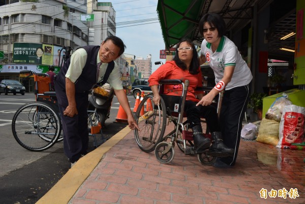 大里區益民路剛完工的通學步道嚴重傾斜，輪椅族一不小心就會翻車，市議員候選人張芬郁（右），台中市身障協會總幹事黃顯堂（左）批評市府不用心。（記者陳建志攝）