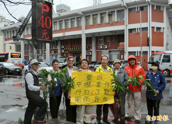 中壢民主事件紀念日推動委員會手持海報及百合花邀請居民風雨無阻參加紀念中壢事件活動。（記者李容萍攝）