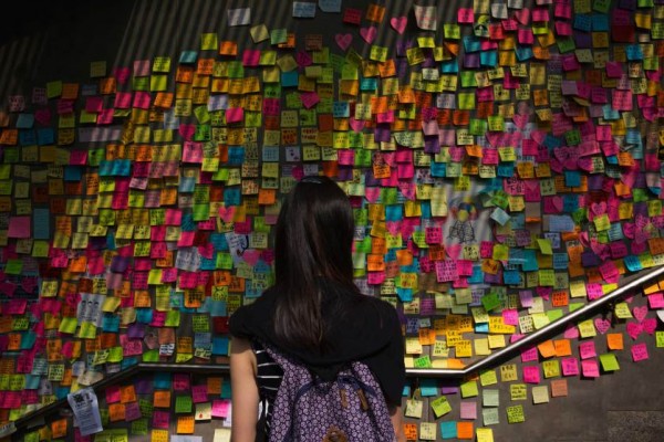 香港政府總部外的「連儂牆」，一名年輕女子站在牆邊，觀看抗議者寫在便利貼上的訴求。（圖擷自《時代》雜誌） 