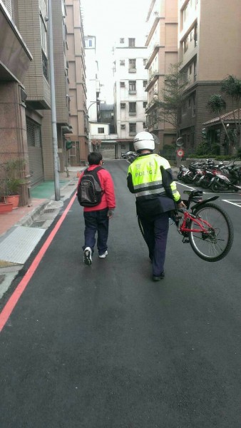 警員唐明福扛著腳踏車，步行陪同男童返家。（記者曾健銘翻攝）