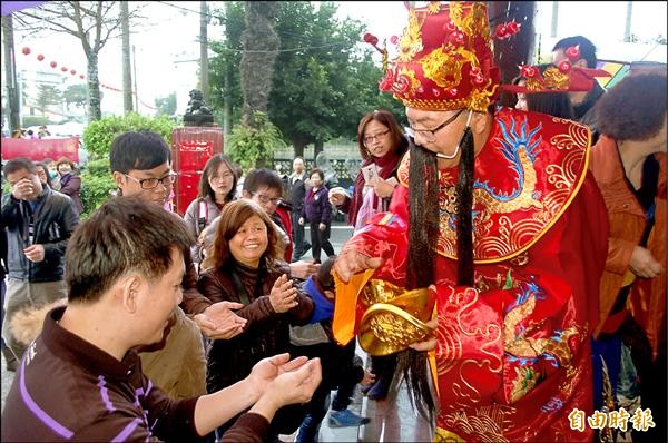 宜蘭市擺厘里長楊德源（右一）巧扮財神爺，發放金元寶造型巧克力，眾人爭相索取。（記者江志雄攝）