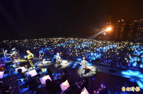 滅火器樂團與高雄市交響樂團共同演出《島嶼天光》，坐在草地上的民眾聽到感動處，一起舉起手機的燈光，現場一片光海，彷彿重現去年3月學運時的場景。（記者張忠義攝）