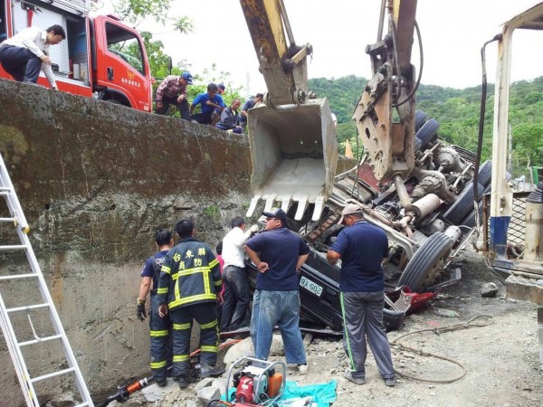 預拌混凝土車翻落擋土牆底，救難人員商請怪手撐穩車頭，再利用油壓器材破壞車門，救出受困的預拌混泥凝土車司機。（記者陳賢義翻攝）