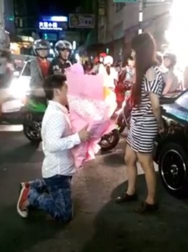 影片中男子雙膝跪地，手上捧著一大束鮮花，對著一名身穿黑白條紋衣服的女子跪著，疑似求婚，只見女子相當尷尬。（圖擷取自臉書） 