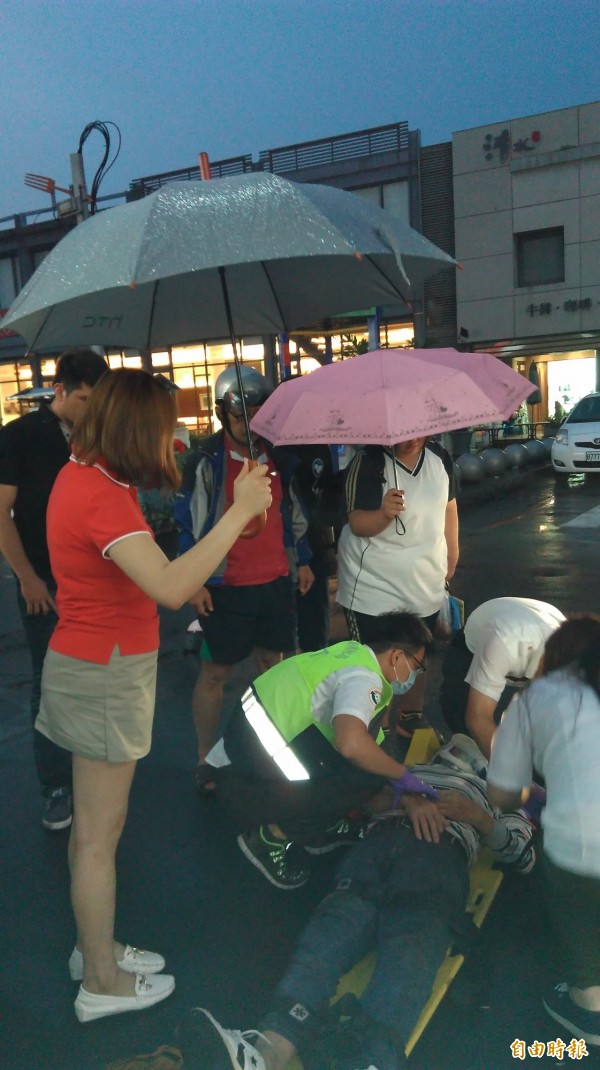 南投市一名男子晚間發生車禍倒地不起，包括一名國中女學生在內的民眾發揮愛心，幫忙撐傘避免淋雨。（記者張協昇攝）