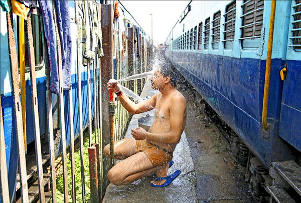 印度連日遭熱浪侵襲，一名火車乘客熱到受不了，竟在賈姆穆（Jammu）火車站的鐵軌間沖起涼來。（美聯社）