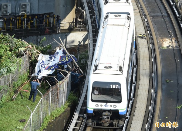 台北市13日下午下起大雷雨，捷運文湖線一輛列車行經萬芳醫院站與辛亥站間，遭緊靠軌道高架橋旁的巨幅廣告招牌倒塌刮中列車右側，所幸無人傷亡，事發後捷運局人員出動移除散落的廣告招牌。（記者廖振輝攝）