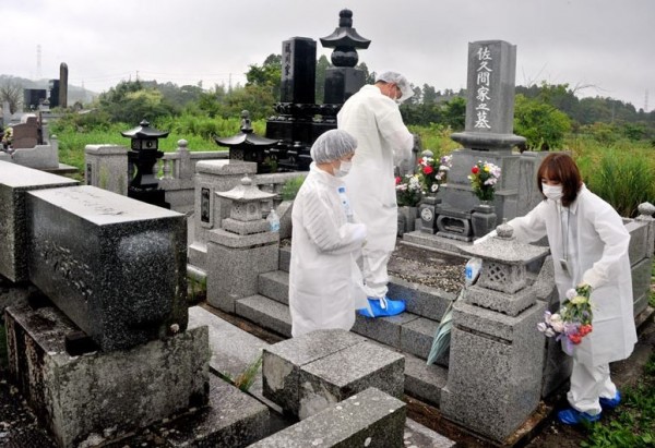 福島核災已過去4年多，今年一樣有災民身著防護服，在盂蘭盆節期間前往鄰近核電站的墓地掃墓。（圖擷自朝日新聞）