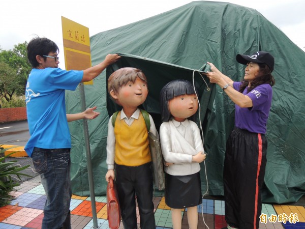 宜蘭縣政府人員，今早到幾米主題廣場，為等車的男孩與女孩人偶穿雨衣。（記者江志雄攝）