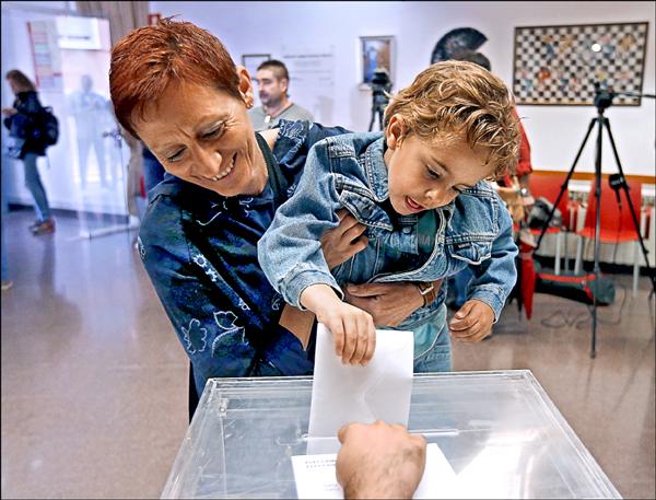 一名小男孩二十七日在巴塞隆納近郊的投票所，幫媽媽投下選票。（路透）