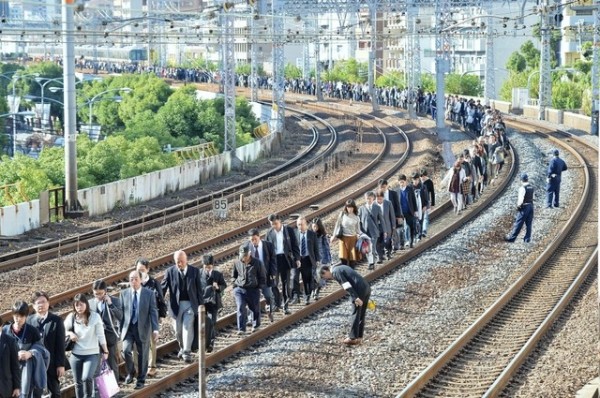 日本JR神戶線今天早上8時發生斷電意外，逾5000名乘客被迫下車行走，鐵道工作人員站在軌道旁向乘客鞠躬道歉，形成特殊景象。（圖擷自《神戶新聞》）