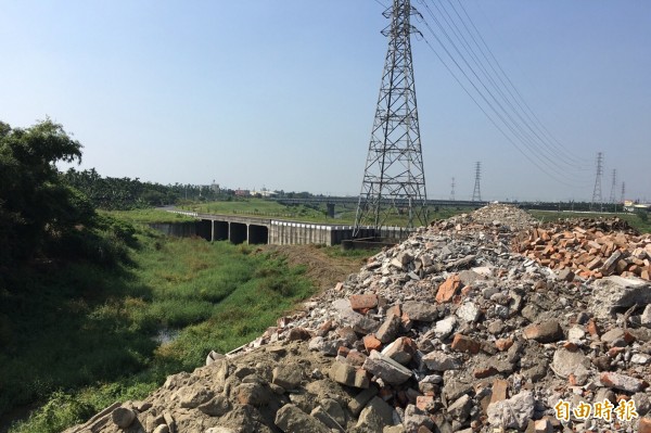 大批建築剩餘土石方，在河道旁堆出近3層樓高的高度。（記者邱芷柔攝）