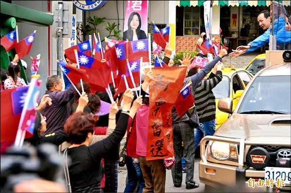 ▲國民黨總統候選人朱立倫昨在南投草屯車隊掃街時，見到路旁大批揮舞國旗的支持者，特別探出身體、伸長雙手與民眾握手致意。（記者陳鳳麗攝）