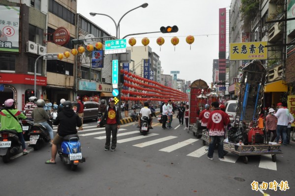 南市北區成功路西向車道被廟會繞境隊伍占用，雖有指揮志工，但機車騎士仍卡在路口、面臨前進方向選擇。（記者王俊忠攝）