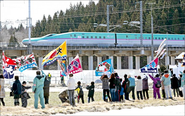 日本北海道新幹線26日正式通車，大批民眾聚集在北海道南端的木古內車站朝新幹線列車揮旗慶賀。（路透）