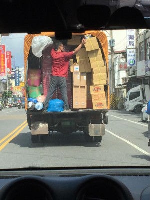 貨車助手站在車斗後方，手扶貨物，完全沒有任何保護機制，顧貨的同時卻忘了顧自己的生命。（圖擷取自爆料公社）