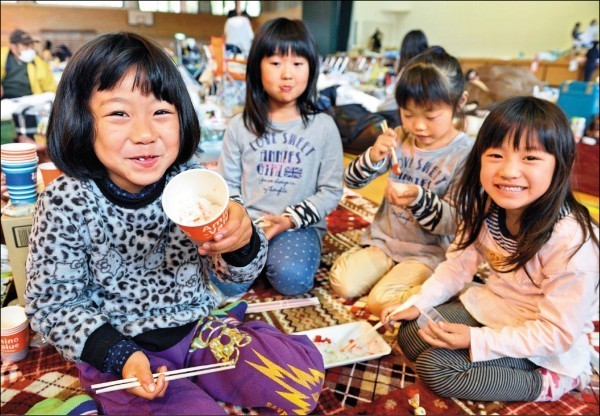 日熊本大地震，暫居避難所的幾位孩童，因吃到食物而開心露出笑容。（美聯社）