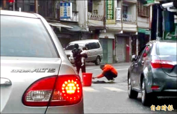 南投縣竹山鎮民黃志成在街頭修補道路坑洞，引來往來人車目光。（記者謝介裕攝）