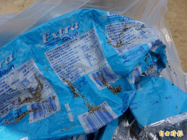 口香糖外袋包材半成品散落在淡水區洲子灣岸上。（記者李雅雯攝）