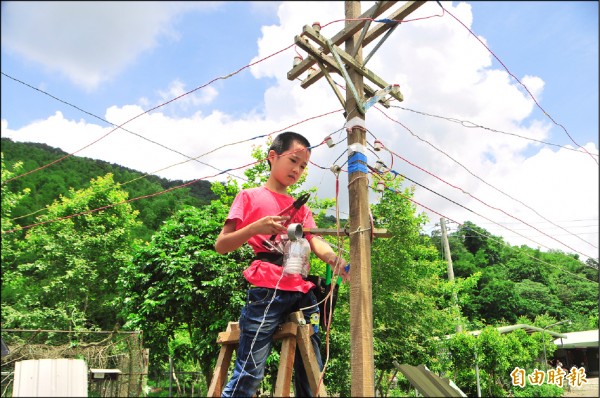 戴菖昱頂著烈日，在外公家的院子修理自製的迷你版電線桿及環保路燈，「因為是興趣，一點都不辛苦」。
（記者花孟璟攝）