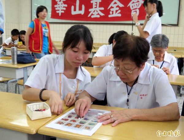 阿嬤戴起眼鏡，在學生幫助下完成拼豆作品。（記者張菁雅攝）