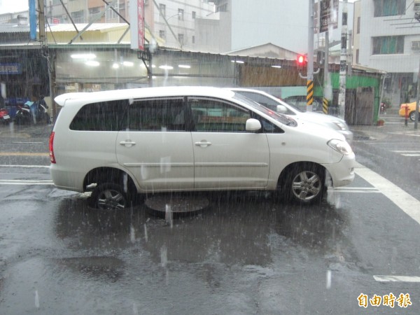 一輛休旅車右後輪卡進人孔洞內。（記者王俊忠攝）