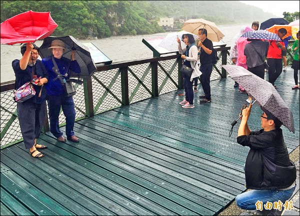 韓國大媽在風雨最大時在太魯閣牌樓前拍照，就連雨傘被強風吹翻了，依舊「淡定」露出燦爛微笑。（記者王峻祺攝）