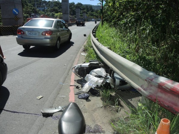 機車遭小轎車攔腰撞，滑進路邊護欄。（記者黃捷翻攝）