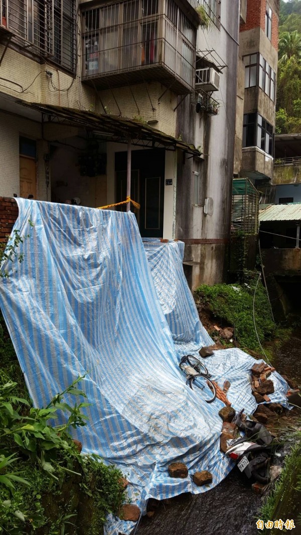 基隆市南榮路393巷緊鄰大排水溝的5樓公寓，路基因受到雨水沖刷，27日晚間突然崩塌，市府先以帆布覆蓋，避免雨水繼續沖刷。（記者俞肇福攝）