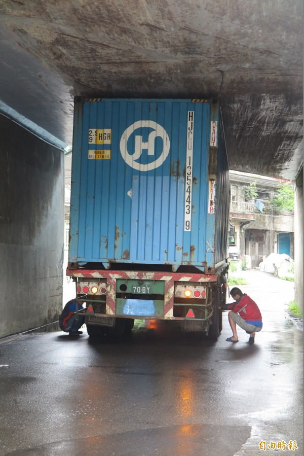 輪胎師傅正在幫貨櫃車洩氣，涵洞上方滿是貨櫃的刮痕。（記者吳政峰翻攝）