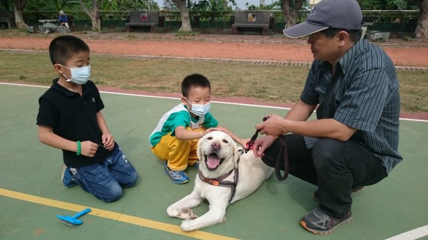 專業人員向學童介紹導盲犬，學童好奇上前摸導盲犬的頭。（圖學校提供）