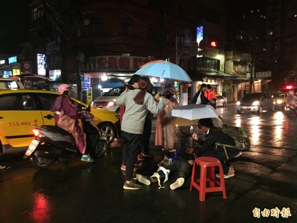 路過的民眾與附近的店家，紛紛拿傘幫倒地的騎士擋雨，令人感到暖心。（記者吳昇儒攝）