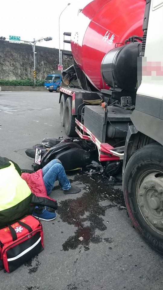 機車卡進砂石車底，騎士在一旁接受消防員包紮。（記者徐聖倫翻攝）

