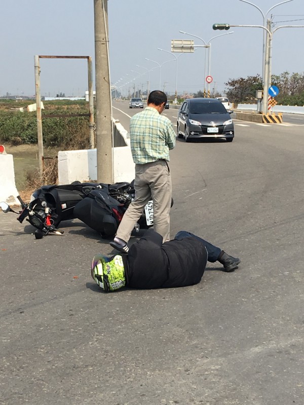 機車騎士倒地不起，路過駕駛（右黑色轎車）停車警戒，肇事駕駛（站立者）查看之後打電話報案。（記者蔡宗勳翻攝）