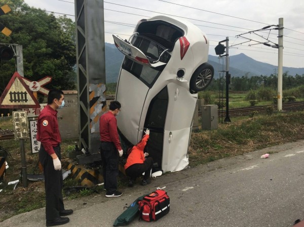 26歲張姓女駕駛開的白色轎車，不明原因撞上平交道限高門柱，因衝擊力道太大，車頭竟「插地」，警消抵達後詢問女子傷勢。（消防局提供）