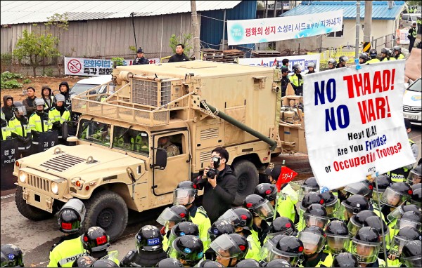 美國軍用拖車廿六日載運薩德裝備駛入星州高爾夫球場，南韓當局出動八千警力開道，以隔開抗議部署薩德的民眾。有抗議者高舉「不要薩德、不要戰爭」標語。（歐新社）