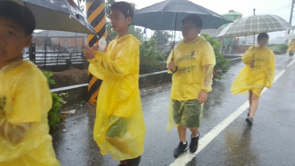 大城鄉西港、頂庄國小畢業生，今日穿著雨衣撐雨傘為公益路跑。（記者陳冠備翻攝）