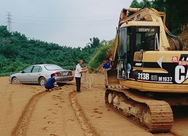 林姓男子駕駛的銀色轎車陷在鳳梨田中，警方聽見有挖土機在附近施工的聲音，立刻請挖土機駕駛協助車輛脫困。（記者曾迺強翻攝）