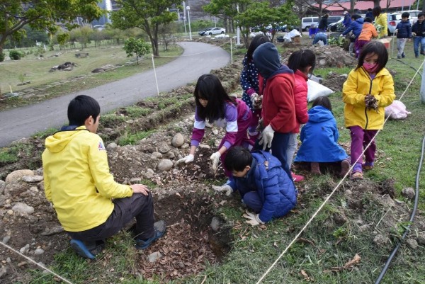 孩童在樹穴中放入落葉和回收廚餘養土，為樹苗準備適合生長的搖籃。（梧桐基金會提供）