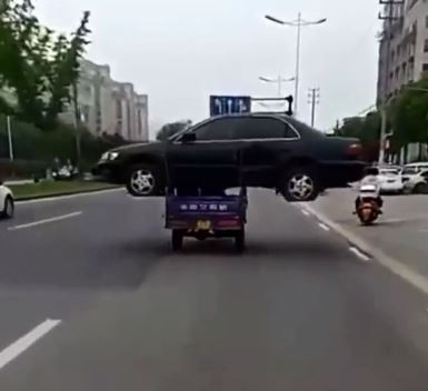 中國浙江有位男子開三輪車載著一輛報廢的黑色轎車上路，結果他佔據了一個車道，也搞得其他車輛不敢靠近，最後交警循線找到司機並向他開罰。（圖擷取自網路）