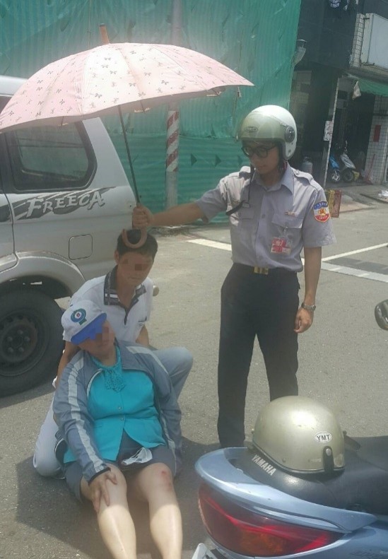 豔陽下老婦車禍路倒，暖警實習生幫忙撐傘。（記者方志賢翻攝）