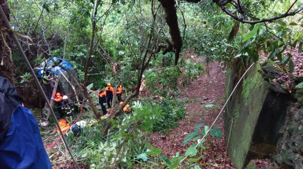 小貨車墜落山谷嚴重扭曲變形，傳出一對夫妻受困，消防員攀繩進入陡峭的山溝搶救，但夫妻倆最後都已身亡。（記者湯世名翻攝）