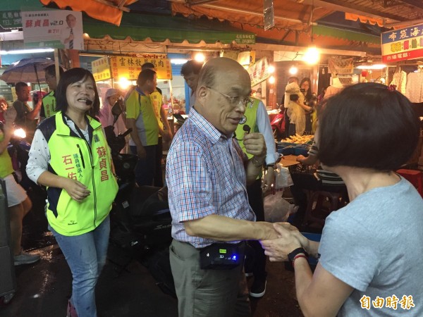 外面下著大雨，蘇貞昌繼續掛著小蜜蜂向菜市場的市民握手。（記者邱書昱攝）